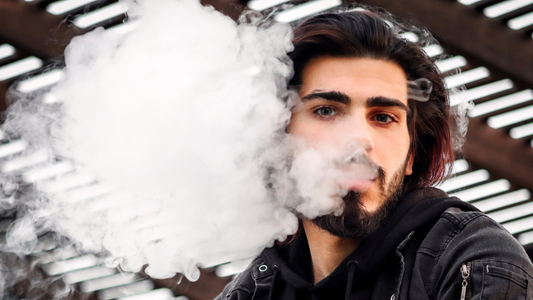 Man with dark hair and beard exhaling a large cloud of vapor