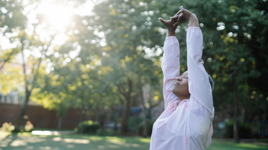 Person stretching outdoors with eyes closed, enjoying fresh air and sunlight