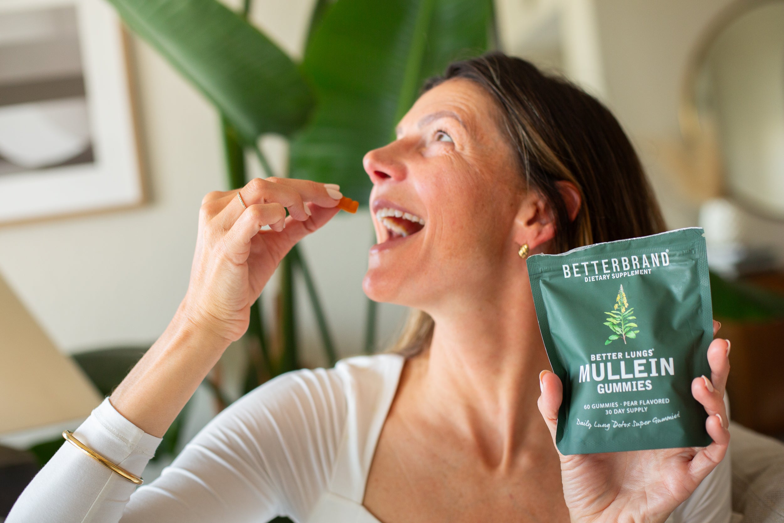 Woman holding a package of BetterBrand Better Lungs Mullein Gummies and about to eat one gummy