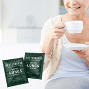 Woman holding a white cup and saucer with Betterbrand Better Lungs Detox Tea packets visible