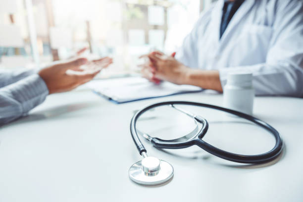 Stethoscope on table with two people discussing in background, suggesting a medical consultation.