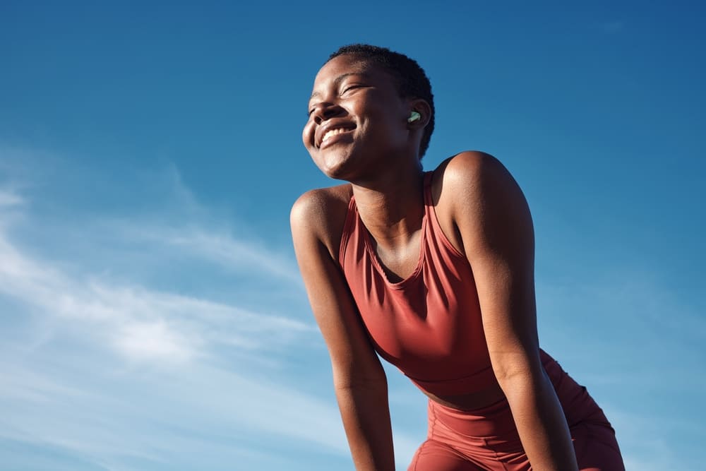 Smiling woman in athletic wear outdoors under blue sky, appearing refreshed and healthy