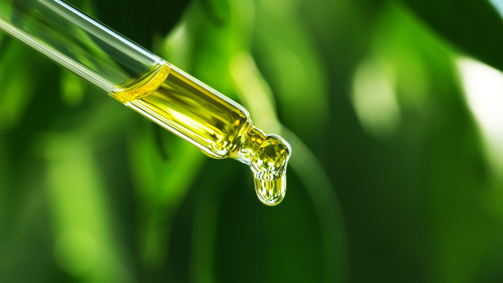 Close-up of a dropper releasing yellow liquid, likely mullein oil, with green blurred background