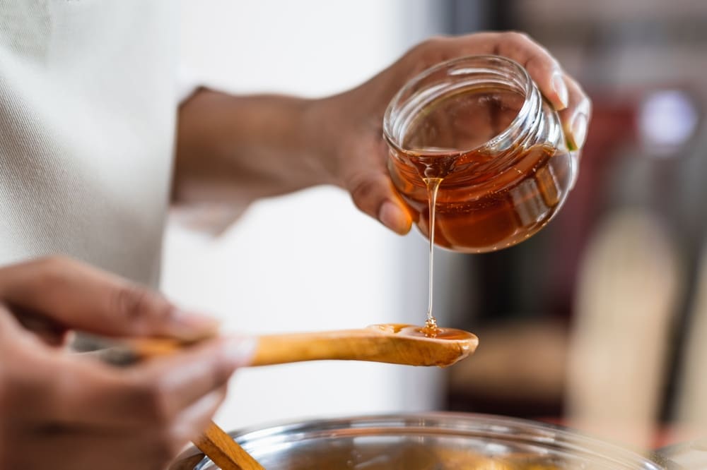 Honey being poured from a glass jar onto a wooden spoon