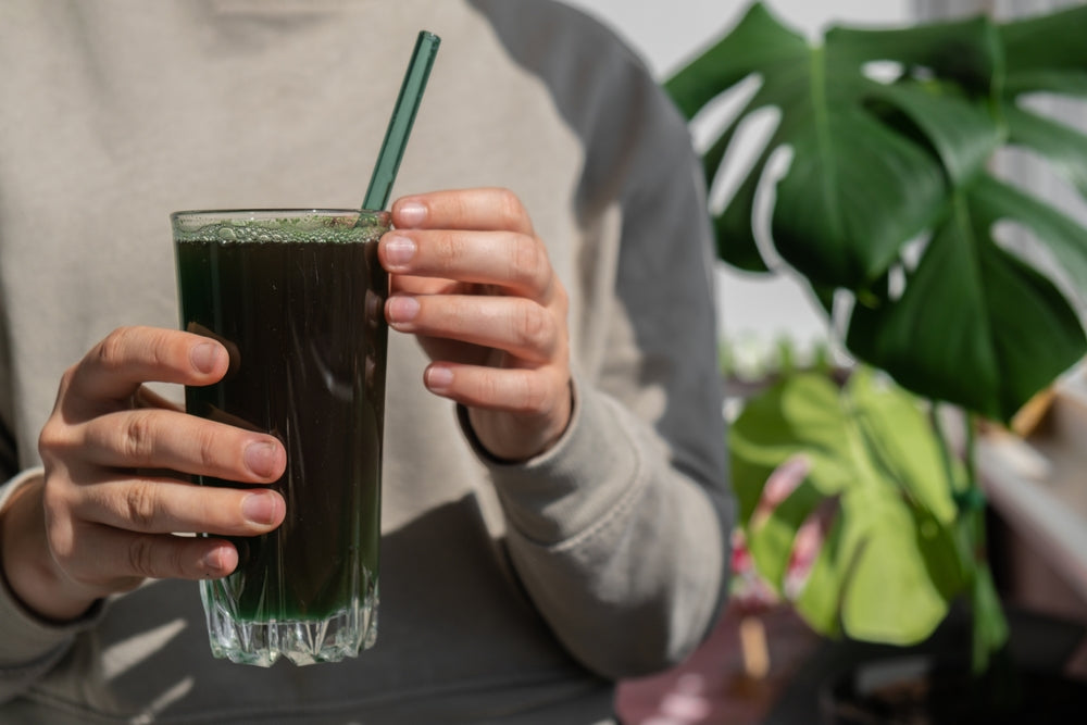 Person holding a glass of dark green sea moss drink with a green straw