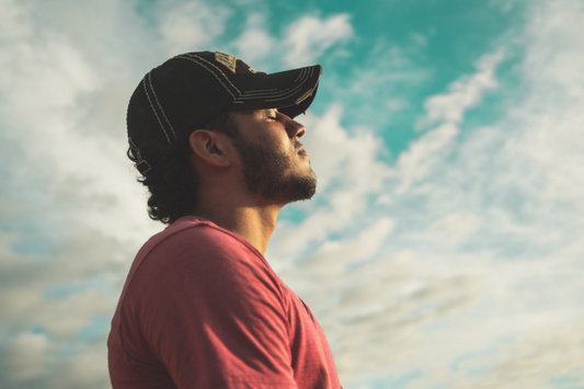 man in coral-colored shirt and baseball cap closing eyes and breathing deeply